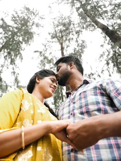 A low-angle shot capturing an intimate moment between a couple, with the tall trees creating a natural frame.