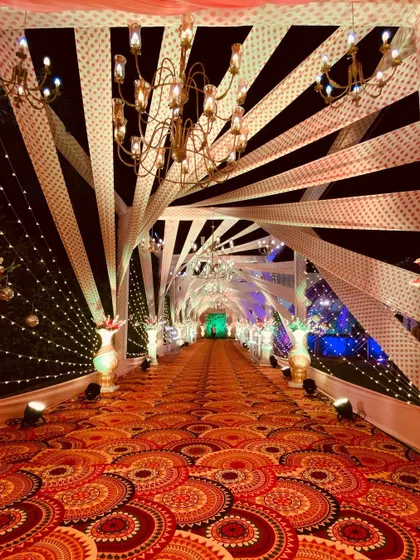 For this Sangeet entrance, I used a dynamic design with crisscrossing fabric strips and elegant chandeliers. The patterned carpet adds another layer of texture and visual interest.