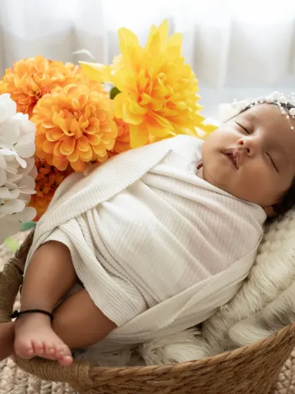 A close-up of a swaddled newborn in a basket, accented with bright yellow and white flowers. We use props and styling to complement your baby's innocence.