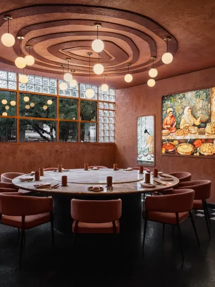 A large communal table at Idylll, set under a dramatic ceiling detail and a cluster of globe pendant lights. This space is designed for shared experiences and celebratory gatherings.