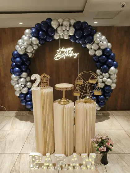 A sophisticated blue, silver, and white theme for Param's 2nd birthday. The full balloon ring, neon sign, and decorative props like a miniature Ferris wheel create a polished and celebratory look.