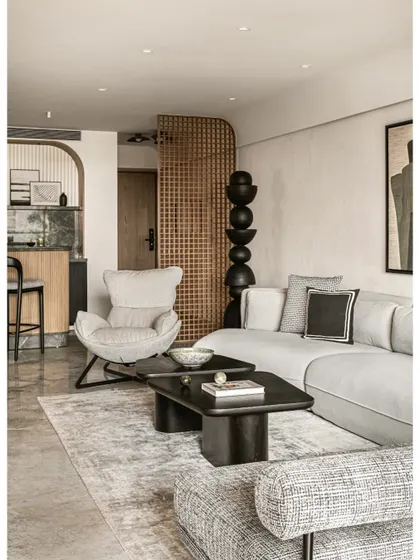 A view from the entryway shows how a wooden grid partition creates a sense of arrival. It offers a tantalizing glimpse into the living area, where a sculptural black totem and a comfortable lounge space await.
