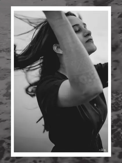A black and white portrait of a woman with her eyes closed, hair blowing in the wind, set against the ocean waves. It's a moment of pure, uninhibited freedom.