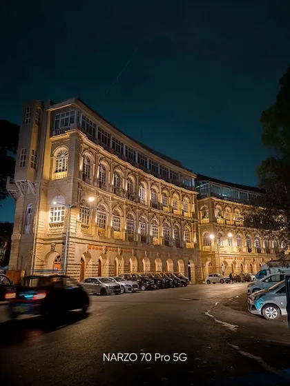 A low light shot of a historic building in Mumbai, capturing the warm architectural lighting and the motion blur of a passing car.