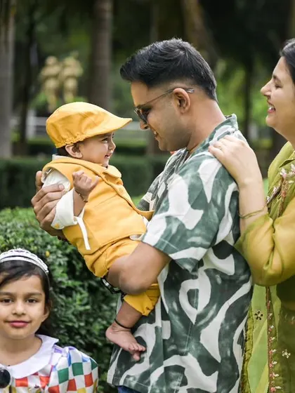 A happy family portrait taken outdoors. The father holds the baby, who is looking at him with a smile, while the mother and sister complete the lovely family group.