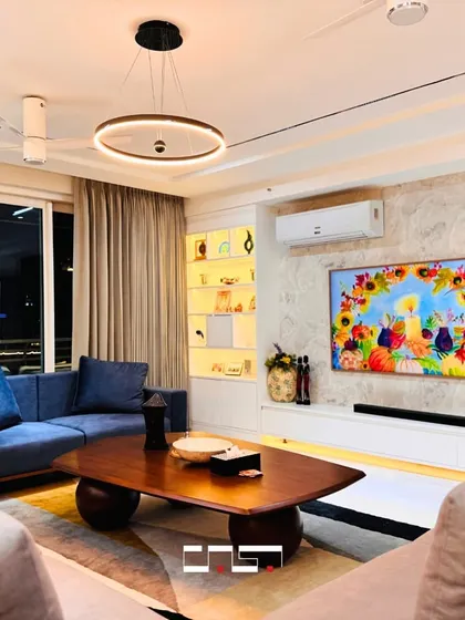 A vibrant living room with a deep blue sofa that provides a beautiful pop of color against a textured neutral wall. The backlit shelving adds a warm glow to the space.