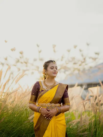 A serene portrait of a bride in a vibrant yellow saree, standing in a field of tall grass at sunset. This shot combines natural beauty with traditional elegance.