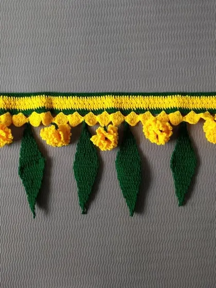 A simple and elegant toran design featuring yellow crochet flowers and green mango leaves. This door hanging is perfect for adding a subtle festive touch to your home entrance any time of the year.