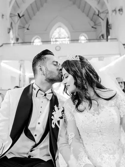 A sweet moment in the church pew, with the groom kissing the bride's forehead. This black and white candid captures the quiet moments of the day.