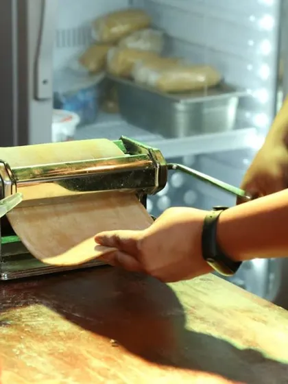 A chef rolling out fresh pasta dough using a hand-cranked pasta machine. This demonstrates our commitment to authenticity and quality, as all our pasta is made from scratch on-site for the freshest possible taste.