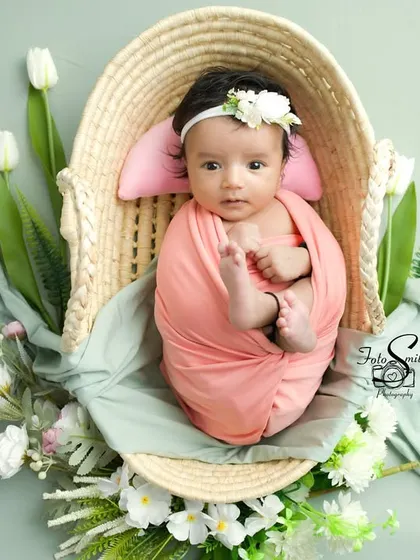 A beautiful portrait of an awake baby in a wicker basket, surrounded by soft fabrics and white tulips. The pastel color palette is soft and dreamy.