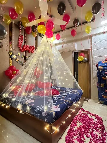 A cozy and romantic anniversary decoration with a fairy light canopy, colorful balloons, and a rose petal pathway.