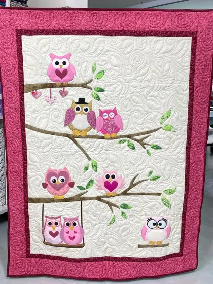 A sweet-as-can-be owl baby quilt. This piece features a family of appliqué owls sitting on tree branches, each with unique details, set against a beautifully quilted background.
