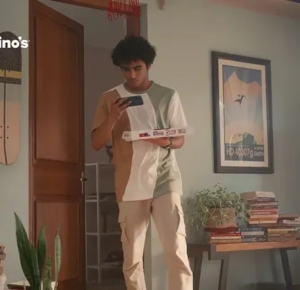 This image shows a character from the Domino's ad entering the room. His two-tone shirt and casual pants are part of a carefully curated wardrobe that feels natural and lived-in.