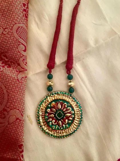 This Tanjore-style pendant is set against a beautiful silk background, showing how perfectly it complements traditional Indian attire.