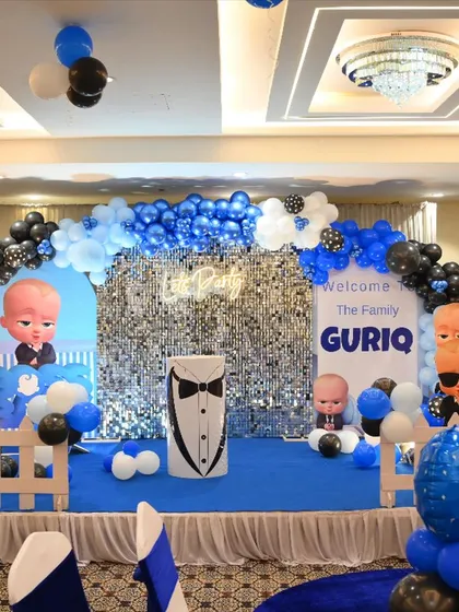 A Boss Baby themed party for Guriq. The stage features a silver shimmer wall, character cutouts, and a blue and black color scheme.