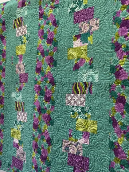 A beautiful quilt in shades of green and purple, with a complex, textured quilting pattern.