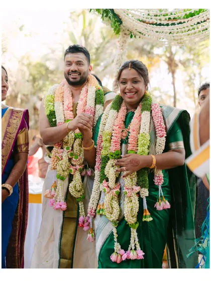 The bride and groom, adorned in beautiful garlands, walk hand in hand during their South Indian wedding ceremony. Their joyful expressions capture the happiness of this significant moment.