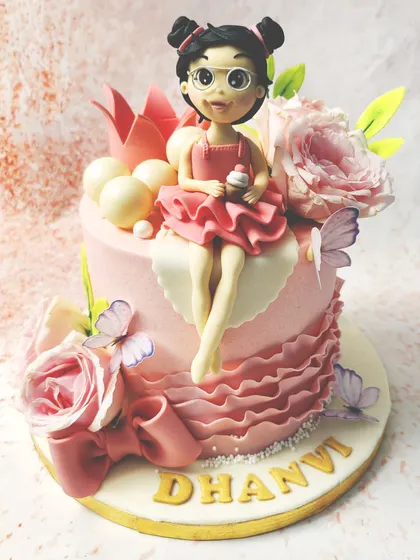 We design a cake fit for a modern princess. A custom-made fondant girl with glasses and a pink dress sits among fresh roses, delicate butterflies, and a pink crown, creating a personalized and enchanting birthday centerpiece.