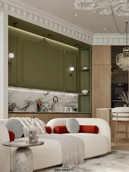 This view shows the beautiful interplay between the plush, curved sofa and the olive green kitchen cabinetry, tied together by intricate ceiling moldings and a classic crystal chandelier.