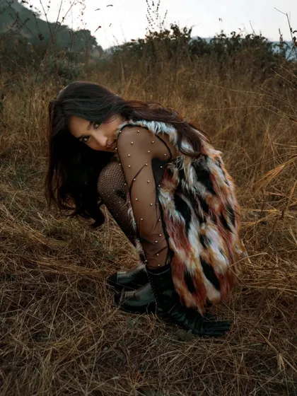 A fashion-forward look shot in a rustic, grassy field. The contrast between the glamorous styling and the raw, natural environment creates a compelling image.