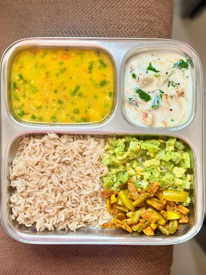 A vibrant vegetarian plate with brown rice, mixed vegetable dal, and a double portion of sautéed snake gourd and ivy gourd, with a side of raita.
