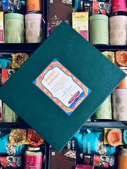The lid of our custom Diwali hamper, featuring a personalized tag, placed over a background of the delicious treats inside.