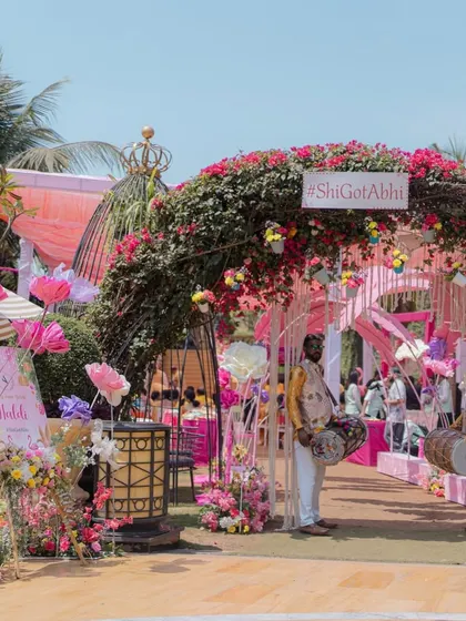 The entrance to a beautiful pastel floral gala. A lush archway of pink bougainvillea and a custom hashtag sign welcome guests to the celebration.