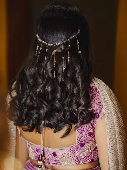 A beautiful hairstyle for a Sangeeth or reception. This look features soft, open curls adorned with a delicate, dangling hair accessory.