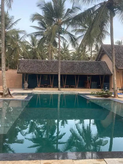 Another view of the Hassan farmhouse pool, reflecting the palm trees and the rustic, earth-toned architecture of the home.
