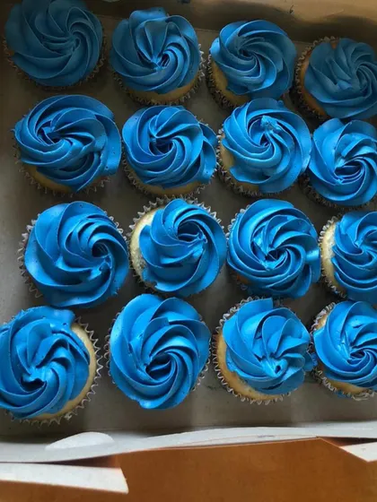 A box of custom cupcakes with vibrant blue frosting, prepared for a baby shower celebration.