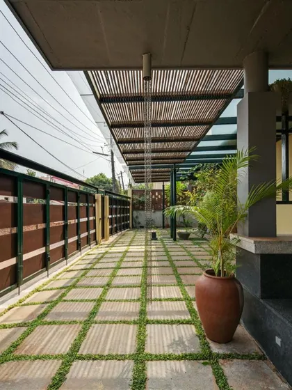 The entrance walkway is a transition space, with a glass and bamboo-slat roof that creates beautiful shadow patterns. The stone pavers with grass joints integrate the landscape directly into the architecture.