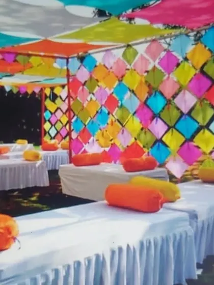 An outdoor seating area for a Mehendi function, featuring a colorful wall made of kites and a canopy of draped fabric.