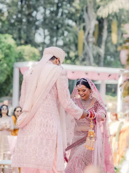 A candid moment from an outdoor wedding ceremony, capturing the couple's interaction as they begin their pheras.