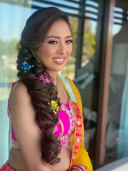 Popping in colors for a vibrant mehendi look. This thick, textured braid is decorated with colorful flowers, creating a joyful and festive hairstyle.