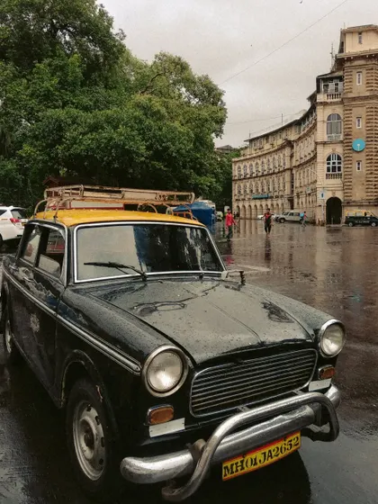 A Kaali-Peeli taxi parked in the rain in front of the historic Horniman Circle. The wet, reflective ground and grand architecture create a beautifully atmospheric and classic Bombay photograph.