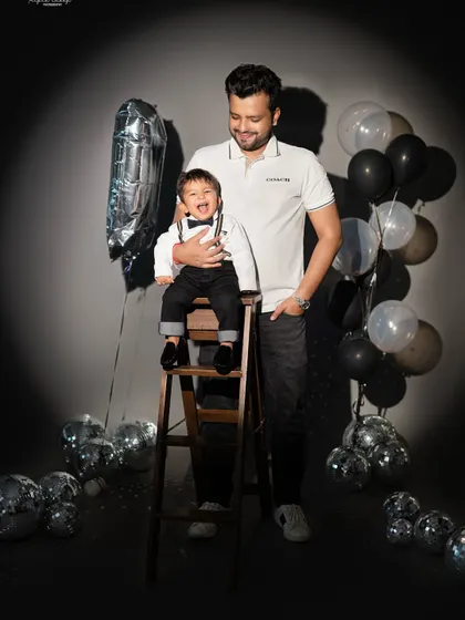 A proud father stands with his one-year-old son on a ladder. This photo captures a sweet moment of support and love during a birthday shoot.