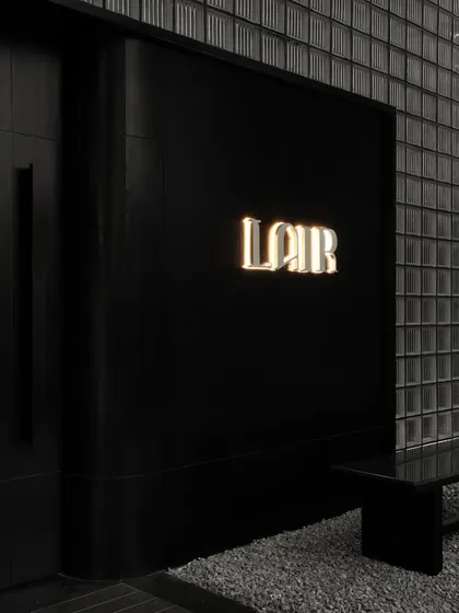 The discreet entrance to Lair, marked only by a softly glowing logo against a black facade and a wall of glass bricks. This is the first hint of the mystery that lies within.