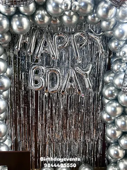 A simple yet festive "HAPPY BDAY" foil balloon banner against a silver fringe curtain. This is a great option for smaller spaces or more budget-friendly decorations.