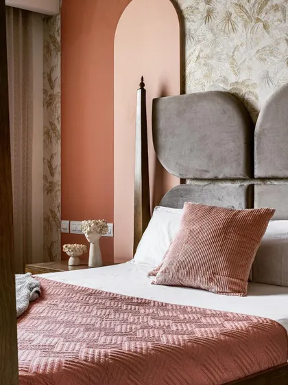 A close-up view of the daughter's bedroom, focusing on the unique headboard and the soft, layered bedding. The color palette of dusty rose and grey, combined with the arched wall detail, creates a sophisticated yet sweet atmosphere.