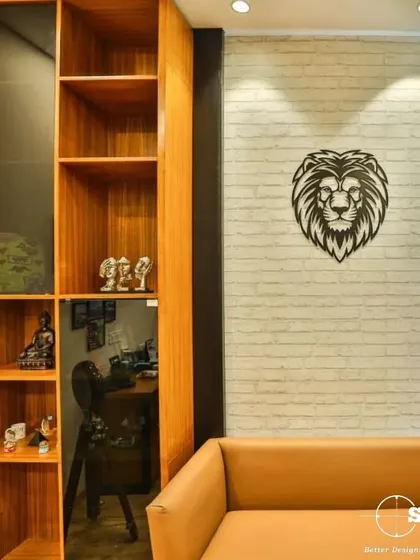 A quiet corner in an office featuring a comfortable leather sofa and a custom wooden shelving unit. A metal lion head wall sculpture adds a touch of personality and strength to the decor.