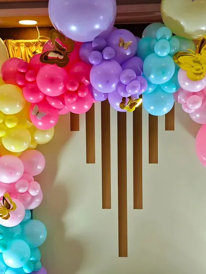 A close-up of a rainbow-colored balloon arch with gold butterfly details, showing the texture and vibrant color combination of the decor.