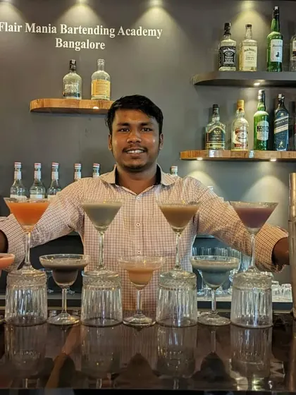 A proud bartender standing behind a bar full of his creations, ready for service.