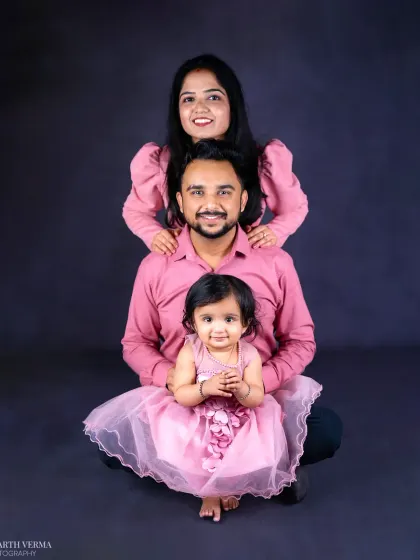 A creative and loving family pose with the parents forming a frame behind their adorable daughter. Their coordinated pink outfits add a sweet touch to the portrait.