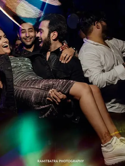 The bride is lifted by friends on the dance floor during a high-energy after-party, her sneakers showing she's ready for fun.