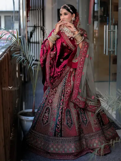 A dynamic pose showing the bride adjusting her velvet shawl. This shot captures movement and highlights the rich fabric and detailed border of her bridal dupatta.