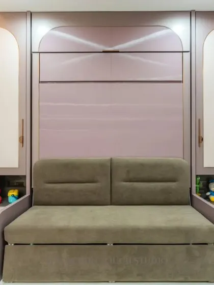 This room features a comfortable sofa that is part of a larger Murphy bed unit. The surrounding cabinetry, with its arched motifs and soft colors, provides ample storage for toys and books, making it a perfect kids' room or guest room.