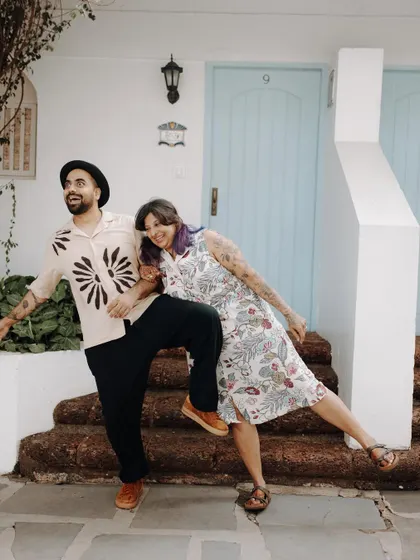 A quirky and fun portrait of a couple in Goa, striking a playful pose on the steps of a colorful villa. It shows their unique personalities.