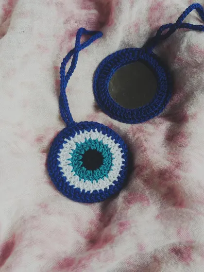 This crochet evil eye bag charm does more than just look good, it also has a small mirror tucked inside for quick touch-ups. It's a unique and practical accessory to hang on your favorite bag.