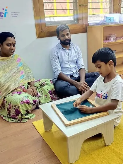 A child practices writing on a small chalkboard while his parents observe. This activity helps develop the fine motor skills necessary for handwriting.